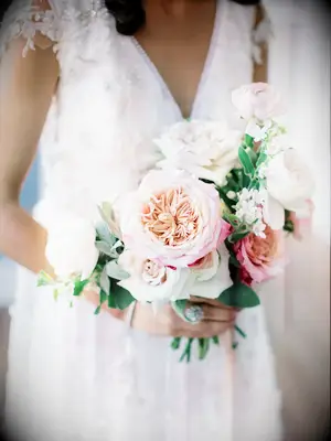 A bride holds a bouquet bursting with flowers of white and pale pink.