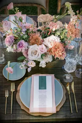 A beautiful table setting sits beneath a riotous floral arrangement in shades of peach and pink.