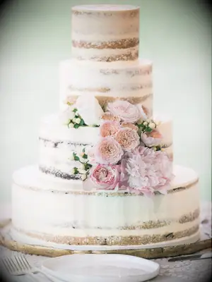 Four-tier rustic wedding cake with semi-naked icing and pink fresh flowers