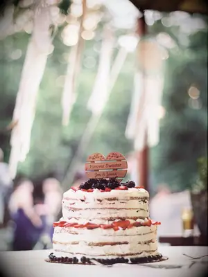 Two-tier rustic wedding cake with fresh berries and custom wood cake topper