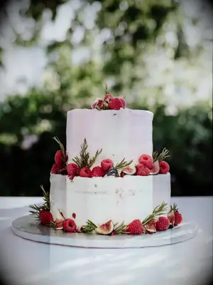 Two-tier rustic cake with white icing covering with fresh berries and greenery