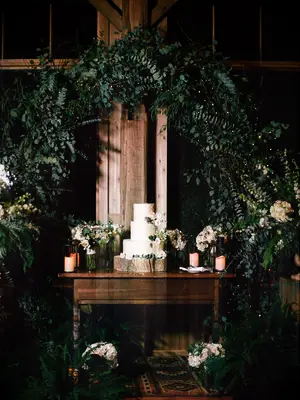 Three-tier rustic wedding cake on tree stump stand under greenery arch