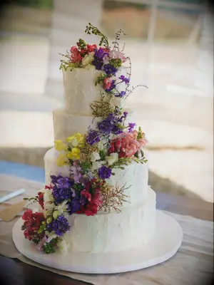Four-tier white rustic wedding cake with cascading wildflowers