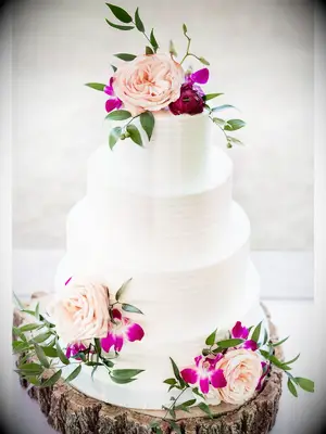 Simple rustic wedding cake with white icing and fresh flowers on tree stump cake stand