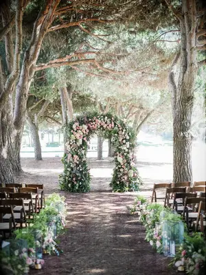 outdoor wedding ceremony in wooded area with floral and greenery arch at the altar