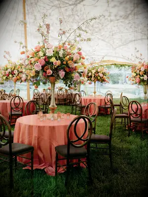 tented wedding reception with round banquet tables decorated with orange tablecloths and tall centerpieces