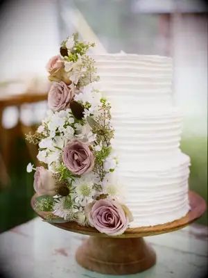 three-tier white buttercream wedding cake with mauve roses, white flowers and eucalyptus