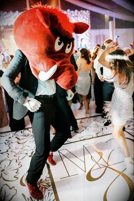 The bride and groom dance together, the groom wearing an enormous mascot mask