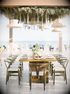 Elegant beach reception with wishbone chairs, wood table and woven chandeliers