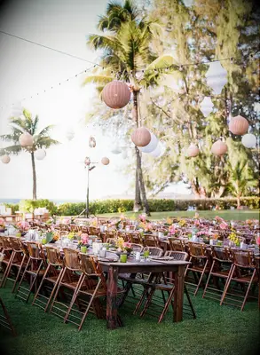 Beach reception with wood tables, bamboo folding chairs and woven chandeliers
