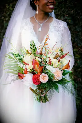 Bride holding tropical bouquet with greenery and orange blooms 