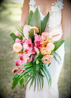Tropical wedding bouquet with leaves, orange ranunculus and pink orchids