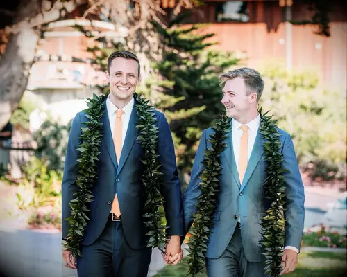 Grooms in blue suits wearing greenery leis