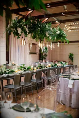 Ballroom wedding reception with tropical hanging greenery and Edison bulbs