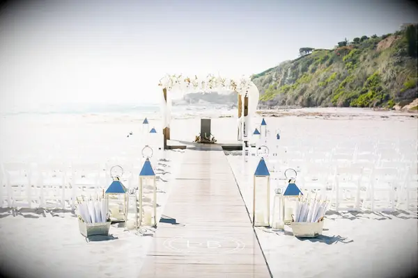 Beach wedding ceremony with white folding chairs, wood walkway and romantic arch