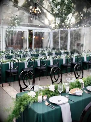 tented wedding tablescape with long banquet tables covered in emerald green linens