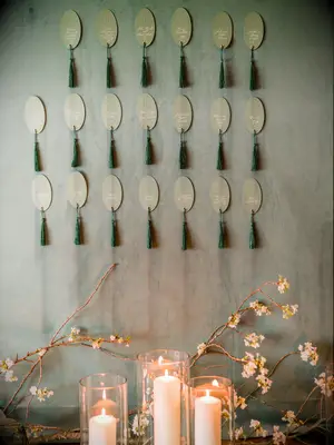 wedding escort card display with tassel cards hanging against sage green wall