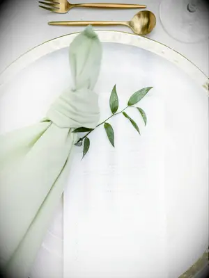 wedding place setting with gold rimmed charger plate and sage green napkin