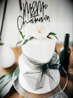 Two-tier white wedding cake with elegant black topper and black tulle bow tie