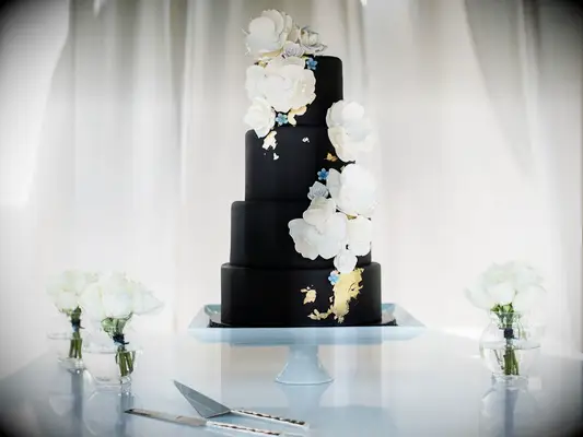Four-tier black wedding cake with gold foil and white flowers