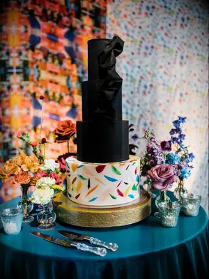 Four-tier wedding cake with three black tiers with fondant ribbon and white base tier with colorful confetti print