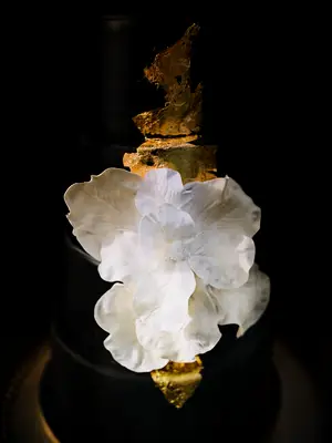 Black four-tier wedding cake with gold foil and large while flower