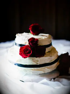 Small two-tier wedding cake with white buttercream frosting and black ribbons and red roses