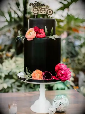 Small two-tier black wedding cake with pink and orange flowers and custom motorcycle cake topper