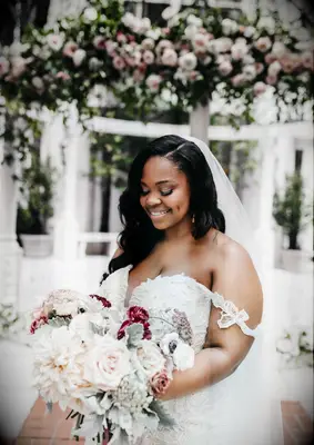 Bride holds a bouquet of white and pink dahlias and roses. 