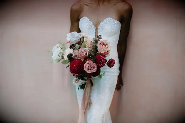 Bride holds a bouquet featuring stunning red dahlias and blush pink roses. 