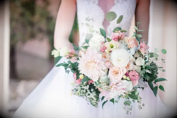 Bride holds a bouquet of pink and white flowers with elegant greenery throughout. 