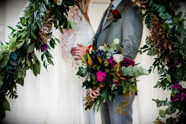 Bride and groom embrace while holding a vibrant bohemian bouquet. 