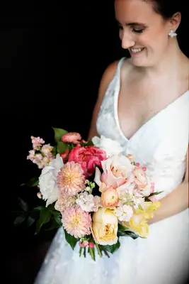 Bride holds a beautiful bouquet of pink dahlias and roses. 