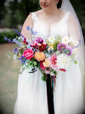 Bride holds a vibrant bouquet of colorful flowers, including purple dahlias. 