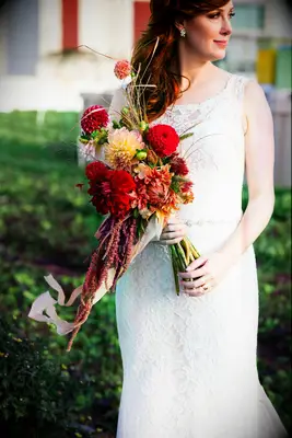 Bride holds a bouquet of vibrant red dahlias. 