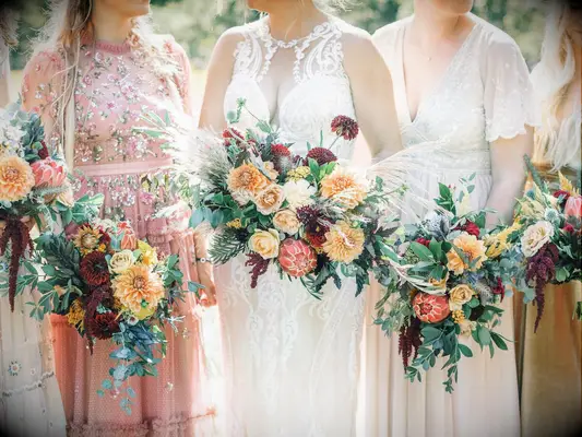Bride and bridesmaids hold bouquets of orange and yellow dahlias. 