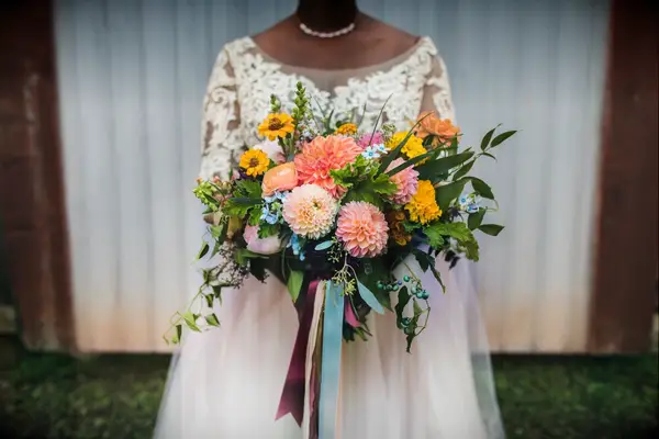Bride holds a colorful and rustic bouquet of pink and orange dahlias. 