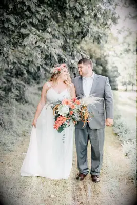 Couple looks at each other lovingly while holding a lush bouquet overflowing with dahlias and greenery. 