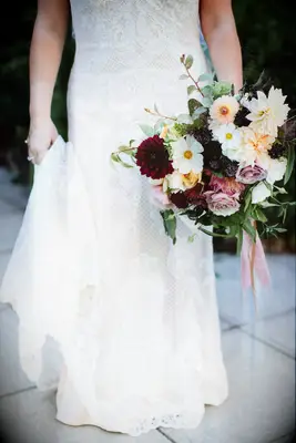 Bride holds a bouquet of dahlias and daisies. 