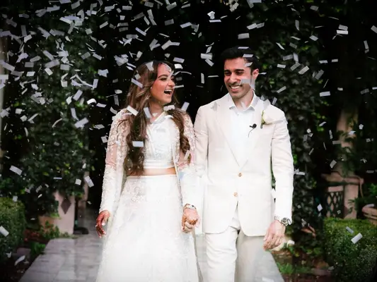 Couple holding hands and laughing under shower of confetti
