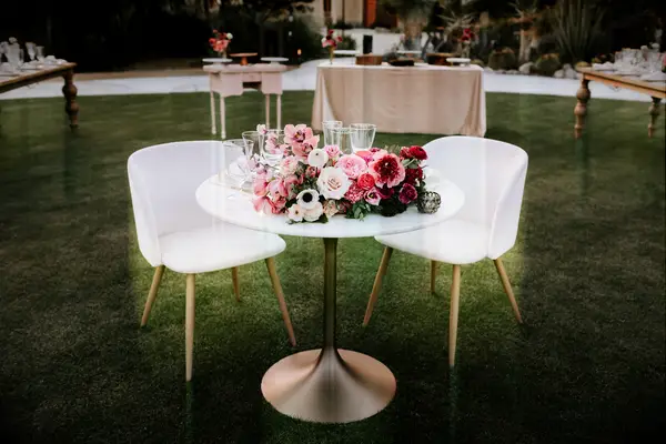 simple wedding sweetheart table with pink, white and red centerpiece and white velvet bucket chairs
