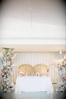 boho wedding sweetheart table decor with rattan peacock chairs and floor-to-ceiling flower pillars with pampas grass
