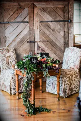 vintage wedding sweetheart table decor with upholstered botanical fabric chairs, greenery garland and wooden mr. & mrs. signs in the middle of the table