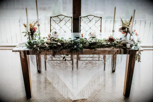 simple boho wedding sweetheart table with vintage lace tablecloth, greenery garland and white taper candles