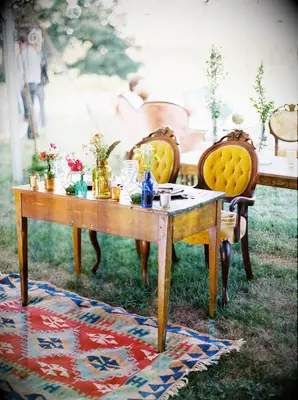 vintage wedding sweetheart table idea with yellow velvet armchairs, vintage glass jars, wooden table and colorful antique patterned rug