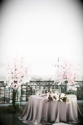 outdoor wedding sweetheart table at rooftop venue with pink cherry blossom trees on either side and city view in the background