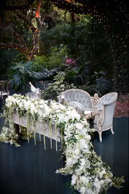 outdoor wedding sweetheart table idea with vintage loveseat and long garland with white flowers and greenery draped over the sides of the table