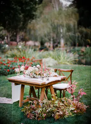 outdoor wedding sweetheart table decor with white gauze table runner, orange taper candles and fall foliage arrangements on the ground