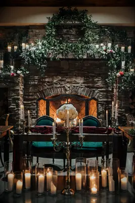 romantic indoor wedding sweetheart table in front of a fireplace decorated with white pillar candles in varying glass vases