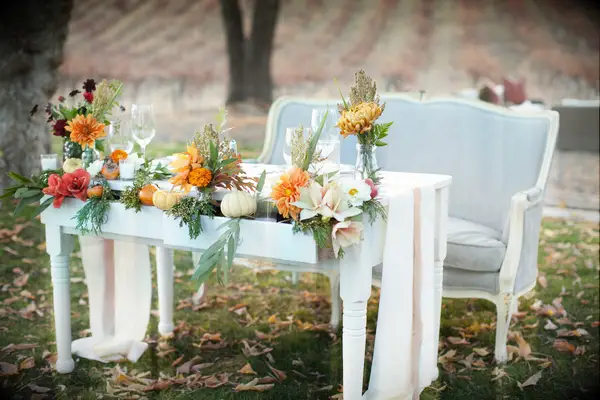 fall wedding sweetheart table idea with light gray vintage loveseat and vintage desk decorated with pumpkins, orange flowers and greenery